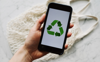 Een foto van iemand die een telefoon vasthoudt, op de telefoon staat het logo van recyclen.
